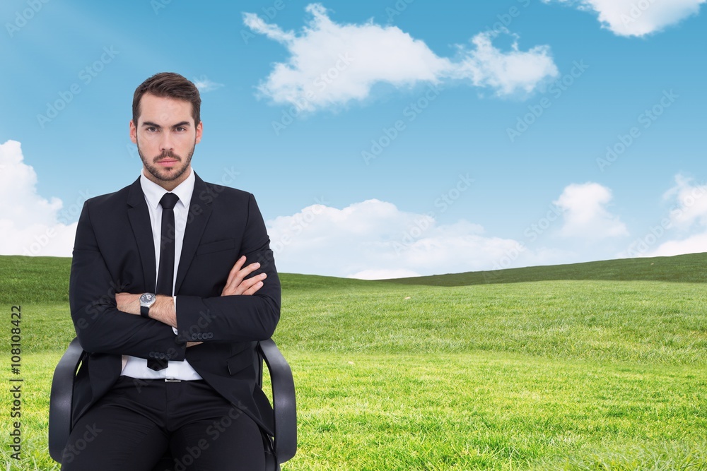 Composite image of serious businessman sitting with arms crossed