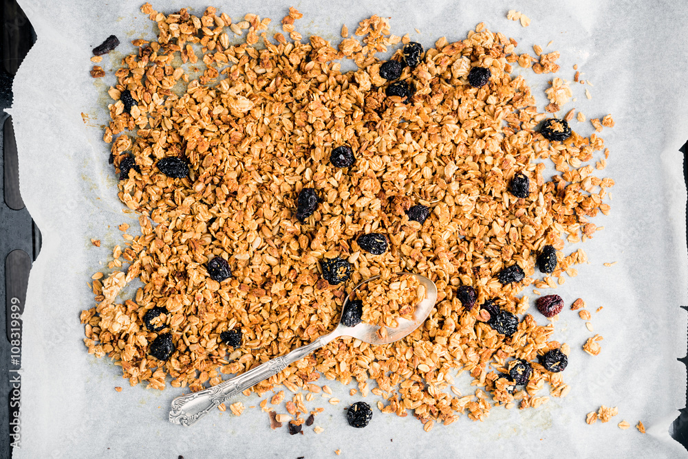 Homemade oat, cherry and coconut granola over baking paper with spoon, 