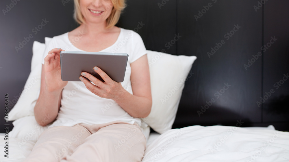 Woman sitting on bed using digital tablet