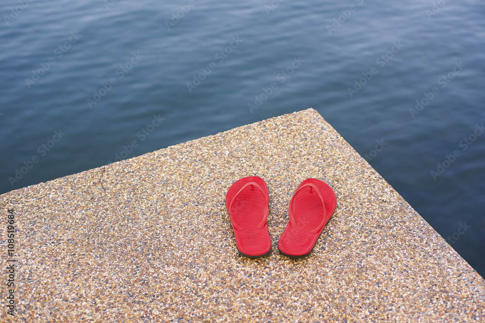 pair of red comfortable slipper placed lake side of stony floor