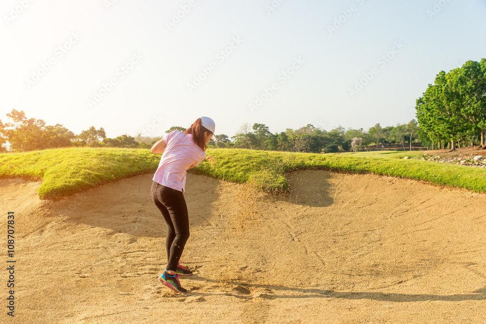 Asain woman golfer hitting golf ball out of a sand trap