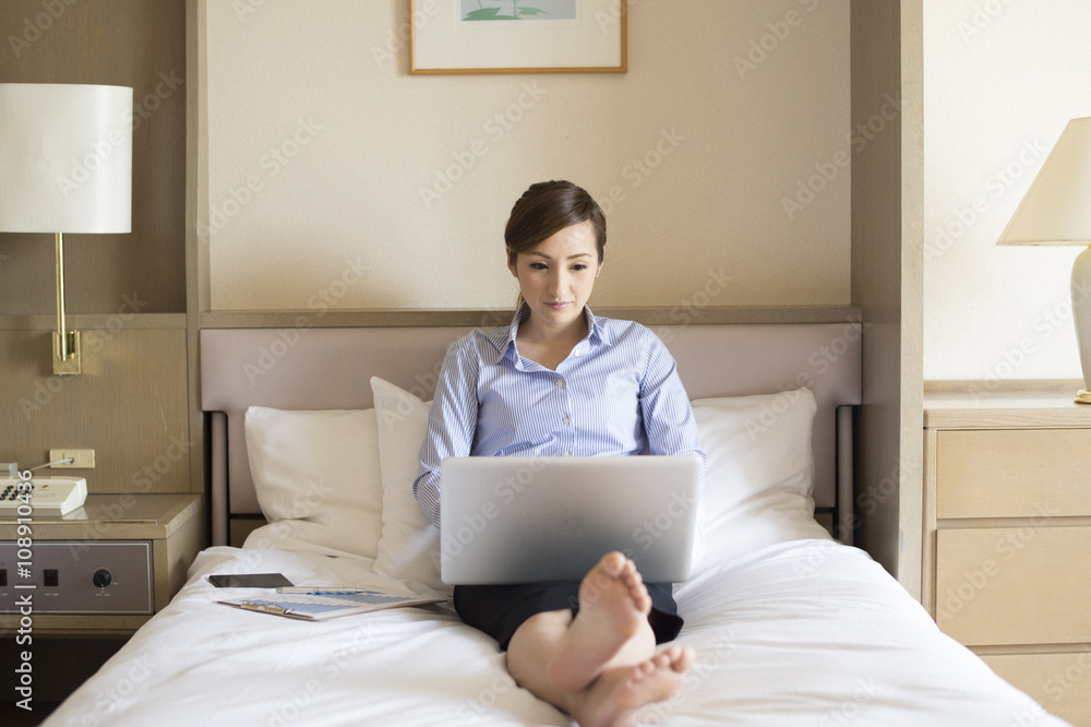 Women have to work on a laptop sitting on a bed in a hotel room