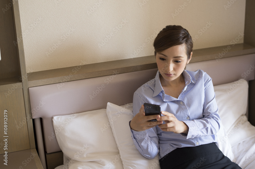 Women sat in business hotel bed, looking at the smartphone