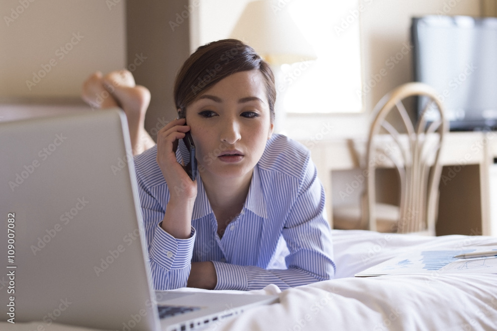 Women are talking on a mobile phone lying face down on a bed in a hotel room