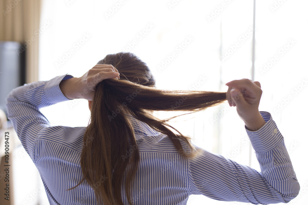 女人坐在酒店房间的床上，把长发扎起来