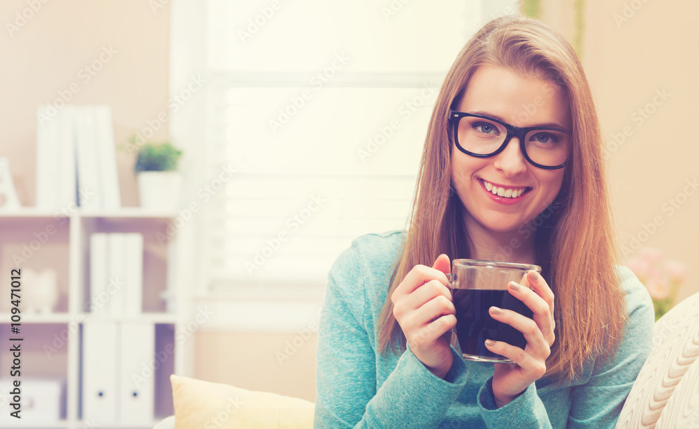 Happy young woman drinking coffee on her couch