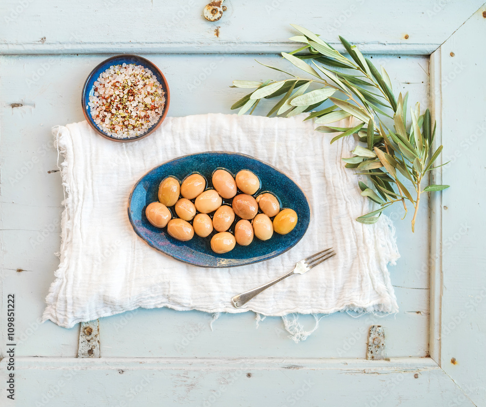 Green big olives in rustic ceramic plate with tree branch and spices