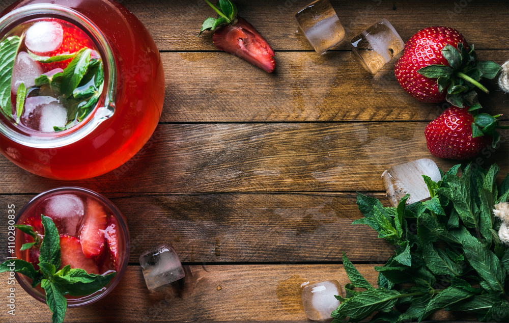 Homemade strawberry mint lemonade served with fresh berries and ice over wooden background, top view