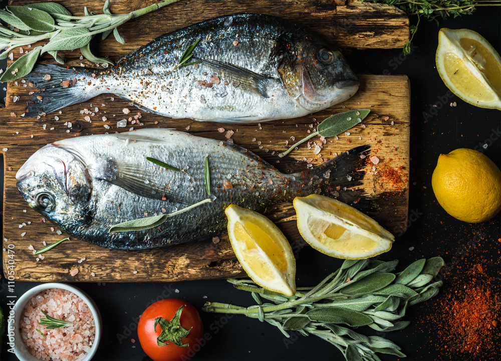 Fresh uncooked dorado or sea bream fish with lemon, herbs, oil, vegetables and spices on rustic wood