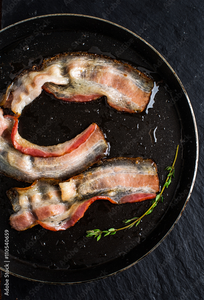 Pan of fried bacon on black slate background