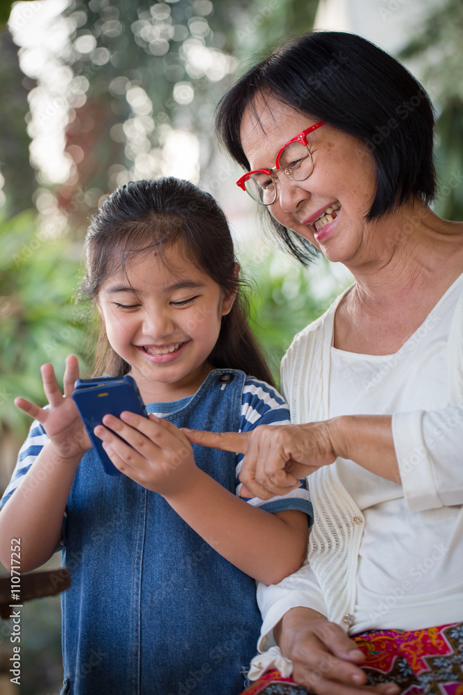 Little Asian girl using mobile phone with her grandmother