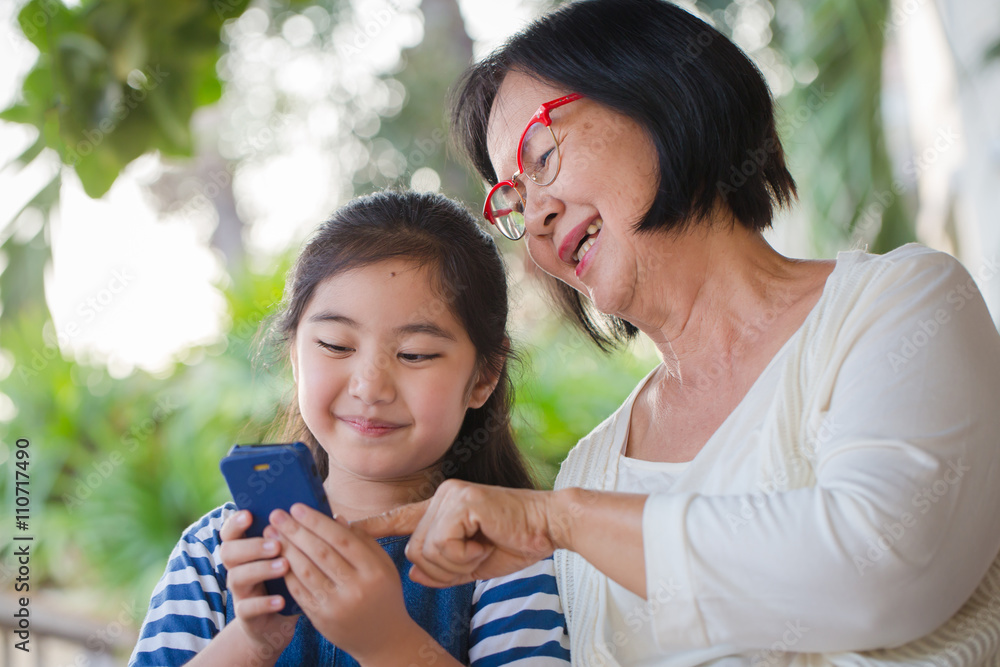 Little Asian girl using mobile phone with her grandmother