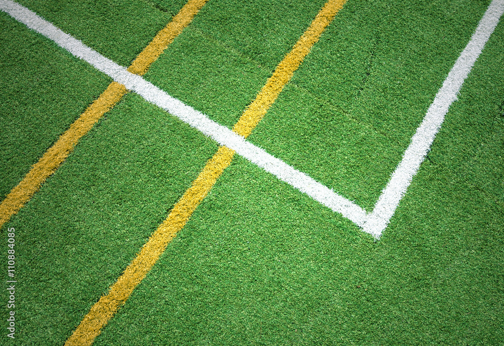 Artificial green grass with white and yellow colored abstract lines on the playground. 