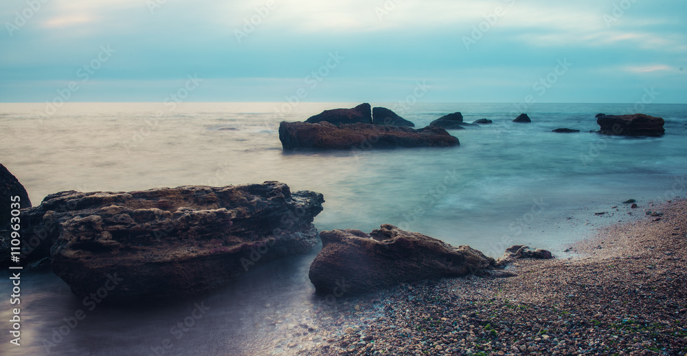 海边有岩石，海水柔软，天空多云，自然季节性的夏季背景，长时间曝光