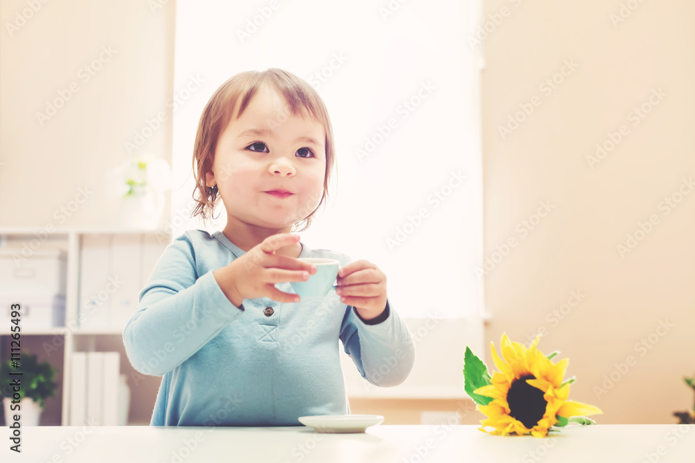 快乐的蹒跚学步的女孩用茶杯喝水