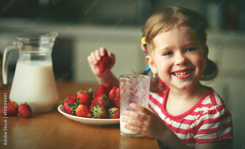 happy child girl drinks milk and eats strawberries in summer hom