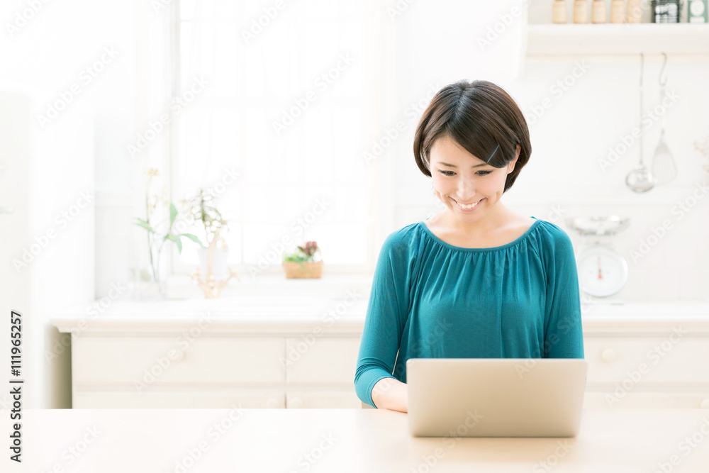 young asian woman using laptop in the kitchen