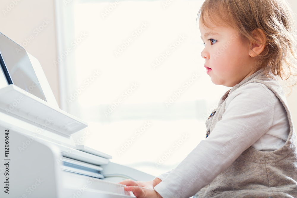 Toddler girl playing the piano with help from her tablet