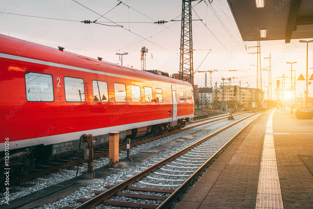 Beautiful railway station with modern red commuter train at colorful sunset in Nuremberg, Germany. R