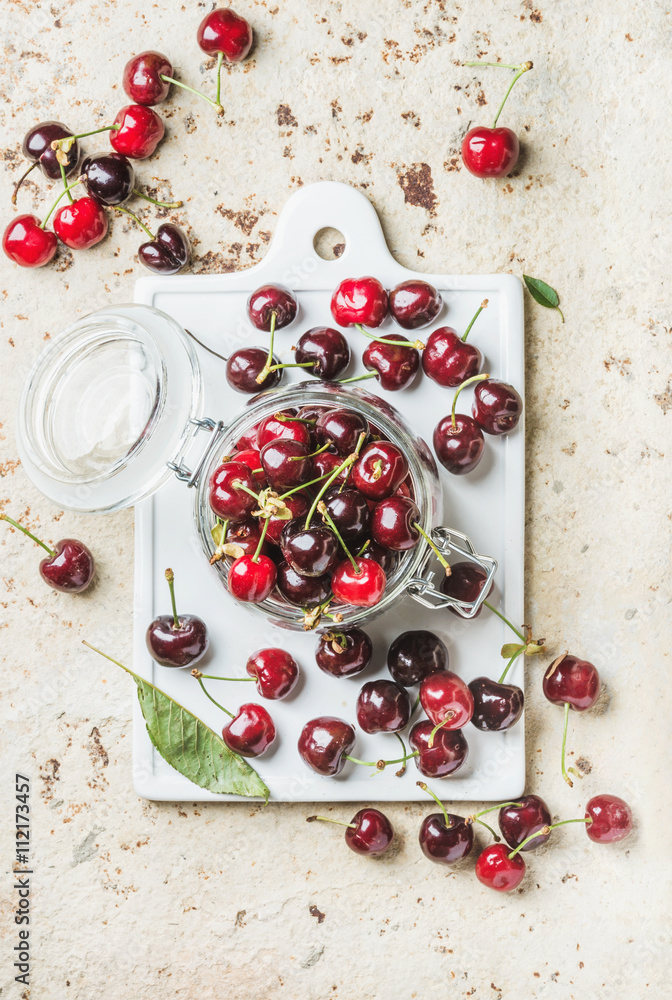 Sweet cherry in glass jar on white board over concrete background