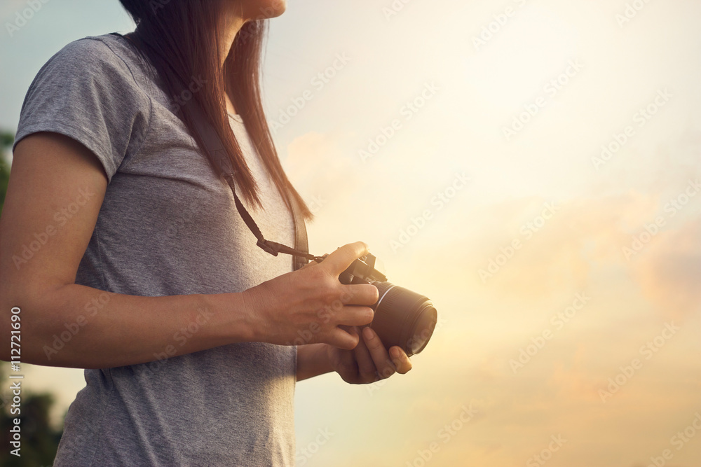 woman holding camera in hands on sunset nature background