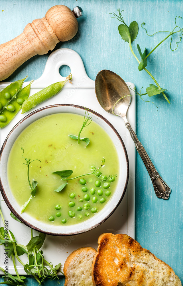 Light summer green pea cream soup in bowl with sprouts, bread toasts and spices