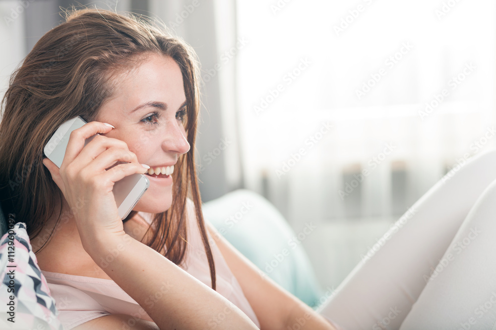 Young woman sitting on couch at home and talking on mobile phone