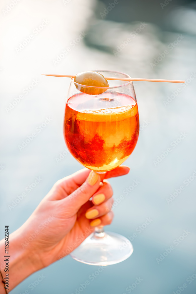 女性手持杯，配Spritz Aperol酒精饮料，水通道上装饰有橄榄