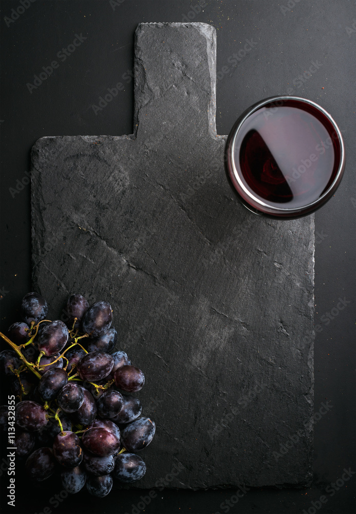 Glass of red wine and grapes on black slate stone board over dark background