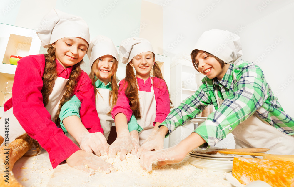 Four friends kneading bakery dough at the kitchen