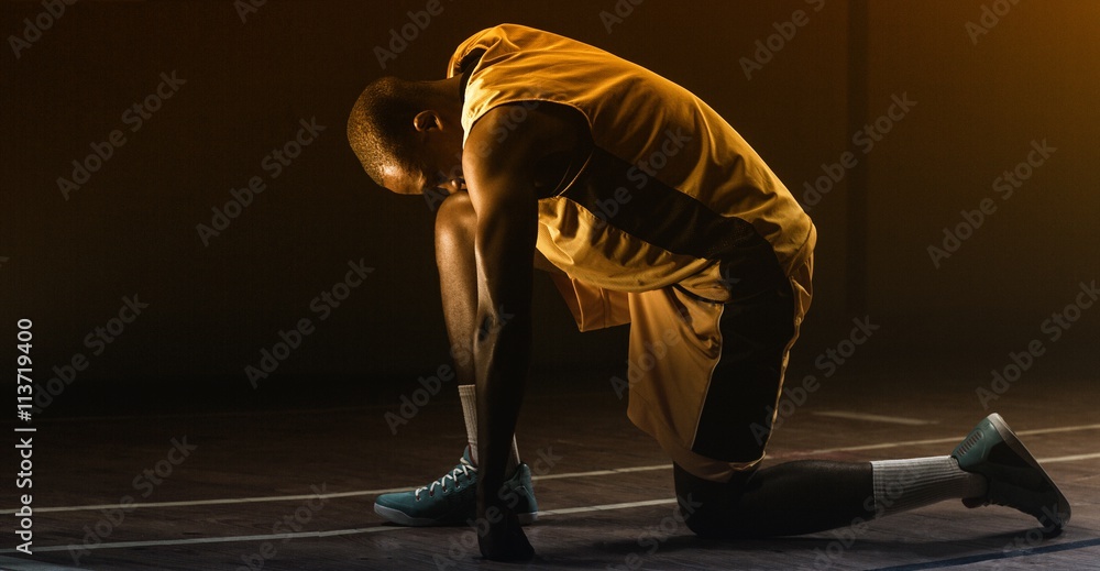 Basketball player preparing to play with knee on the floor and head lowered