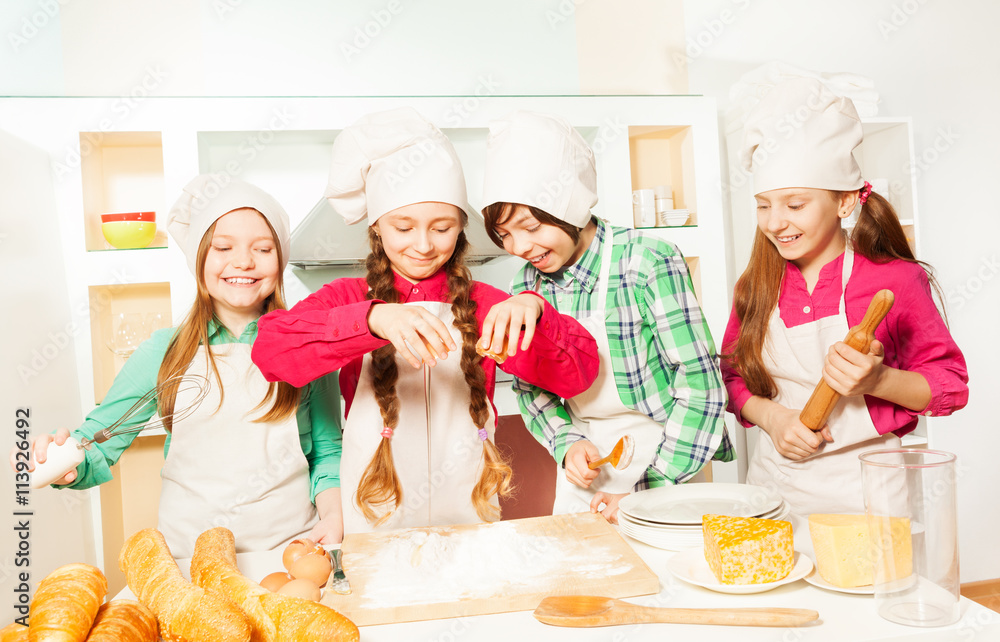 Smiling kids in cooks uniform making bakery dough