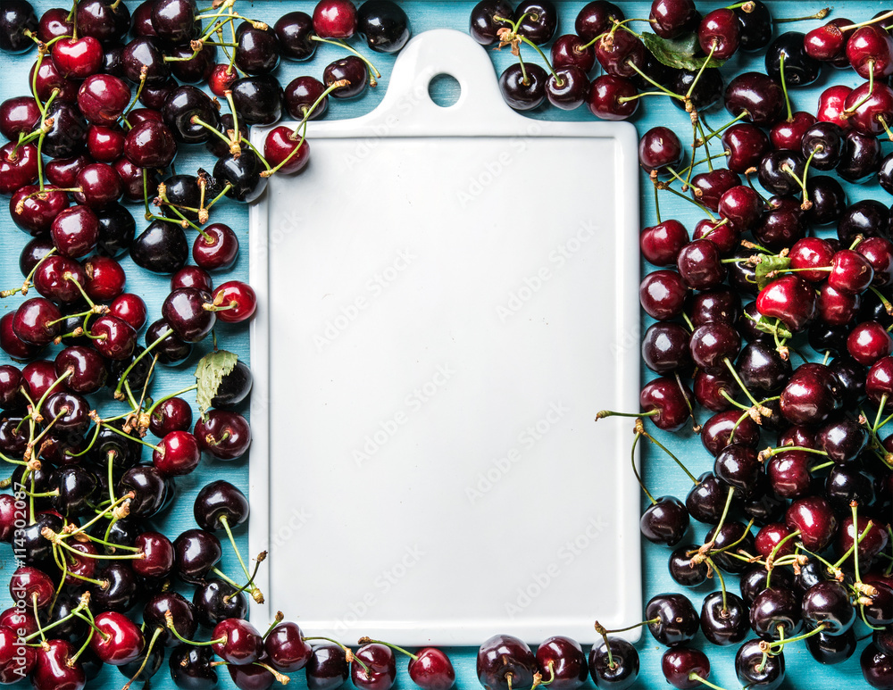 Sweet cherries in blue wooden tray with white ceramic board in center