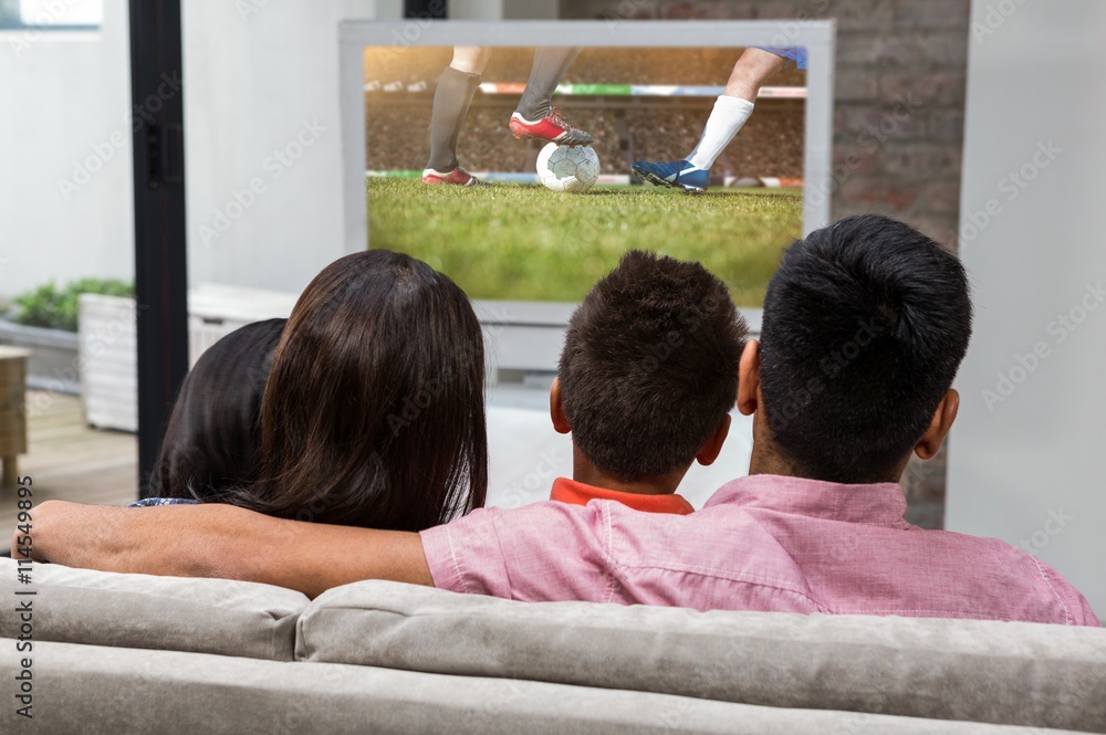 Composite image of happy family watching tv on the sofa