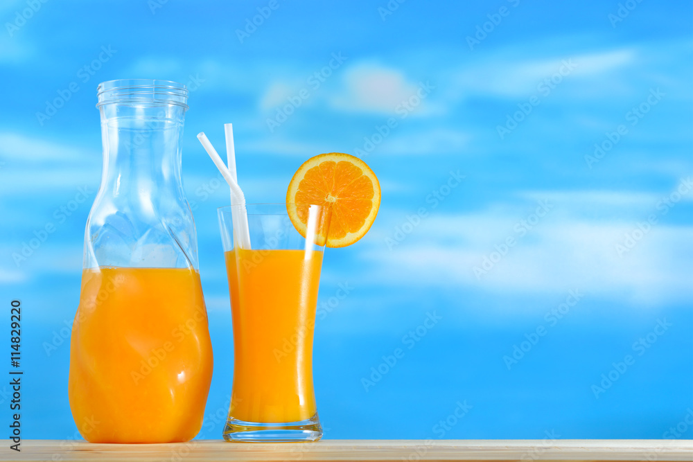 Orange juice in jug and glass on sky background