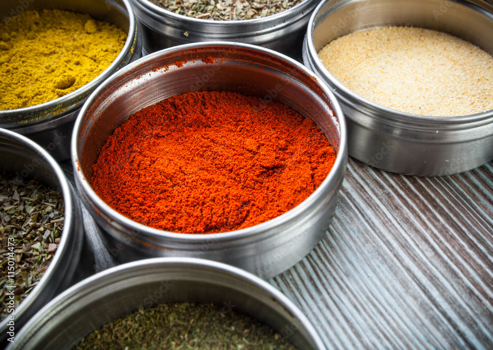 Spices and herbs in metal containers on wooden table