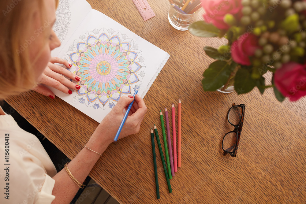 Female drawing in adult coloring book at home