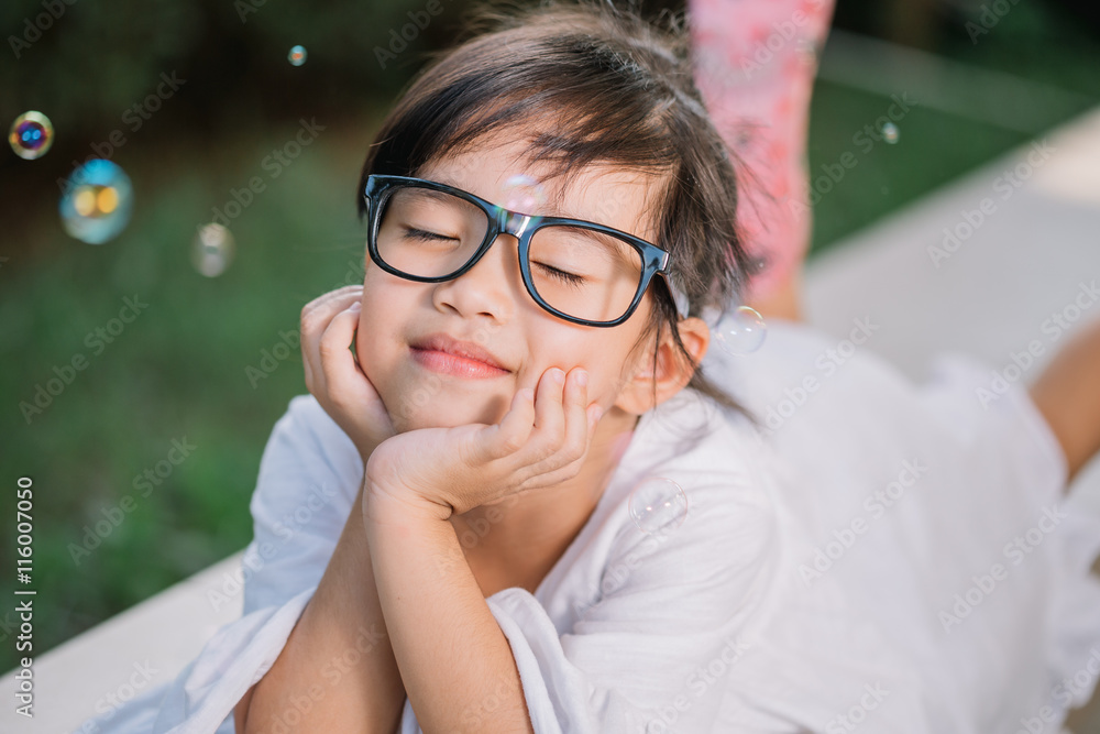 Sweet, happy, smiling five year old girl laying on a grass in a park playing with bubbles and laughi