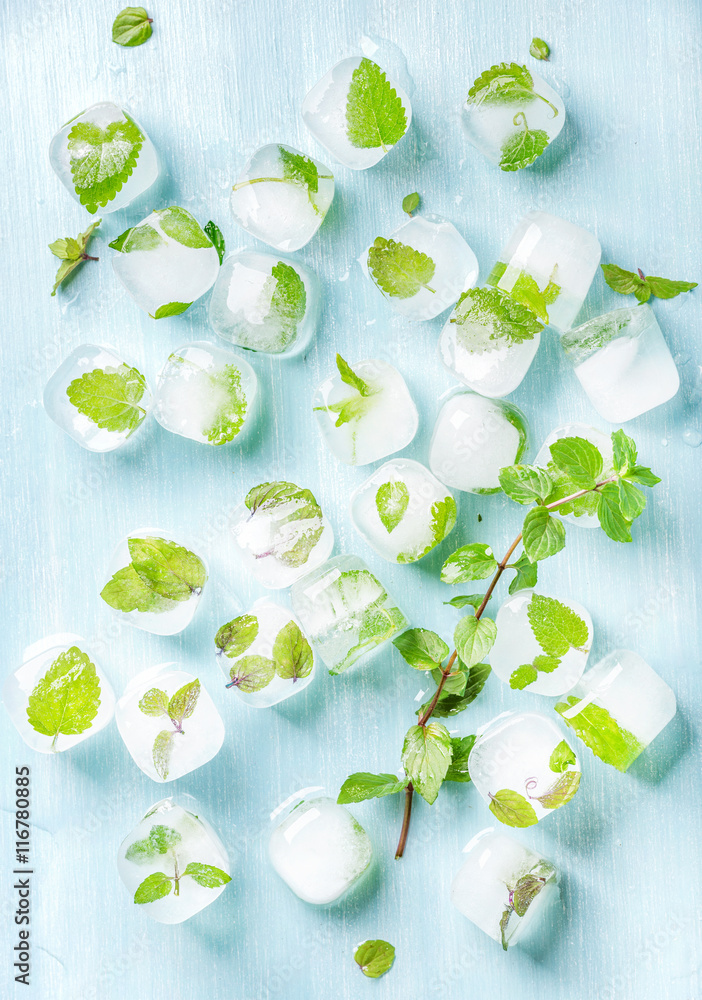 Ice cubes with frozen mint leaves inside on blue Turquoise background, top view, vertical