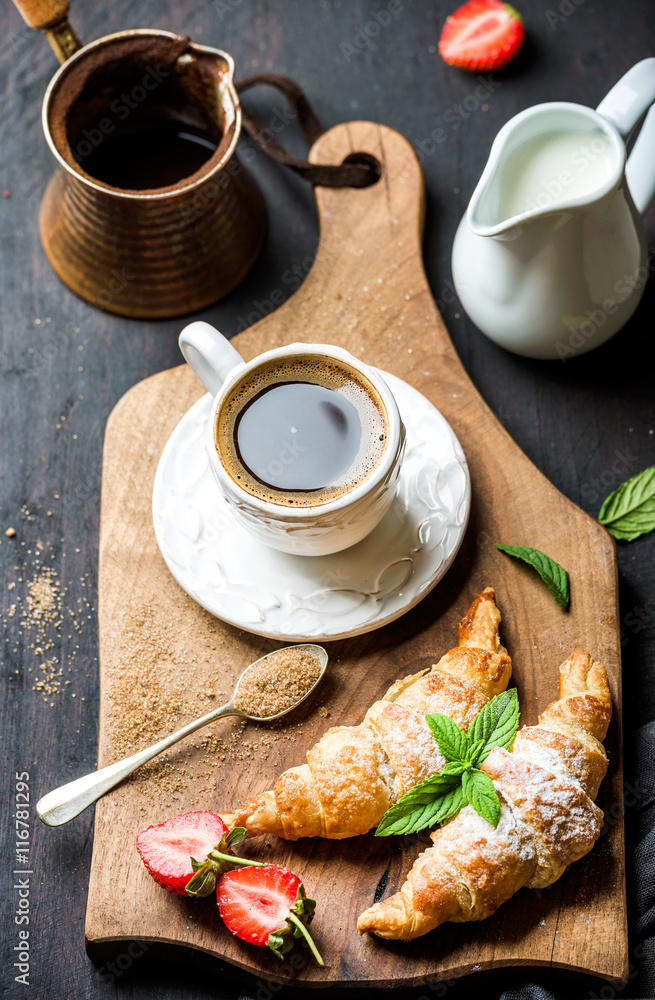 Breakfast set. Freshly baked croissants with strawberry, mint leaves and cup of coffee on wooden boa