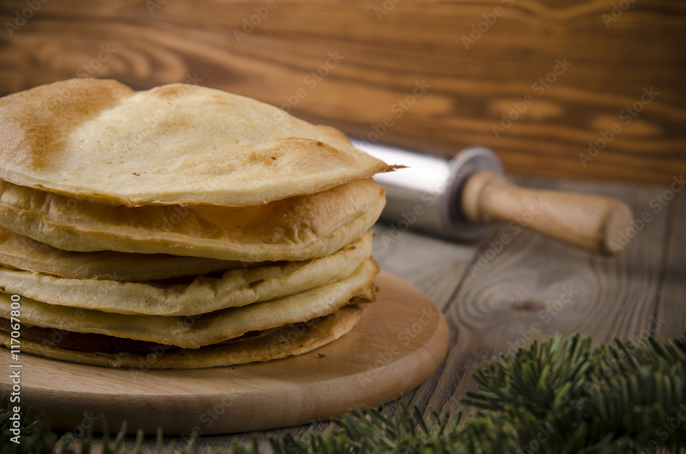 Cakes for the cake napoleon on a wooden background decorated with fir branches and rolling pin