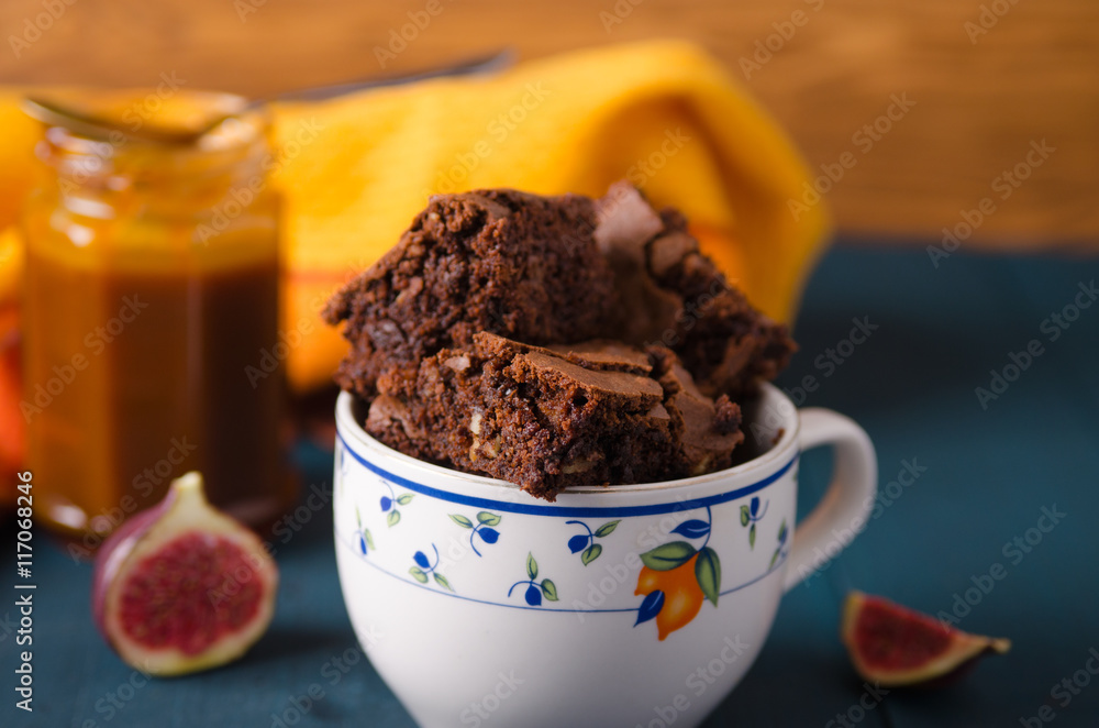 Brownie with walnuts, figs on a dark blue background with a yellow tablecloth in a white cup with bl