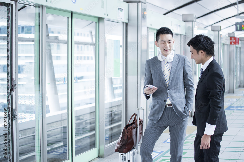 Two young businessmen have a stand talking at the station