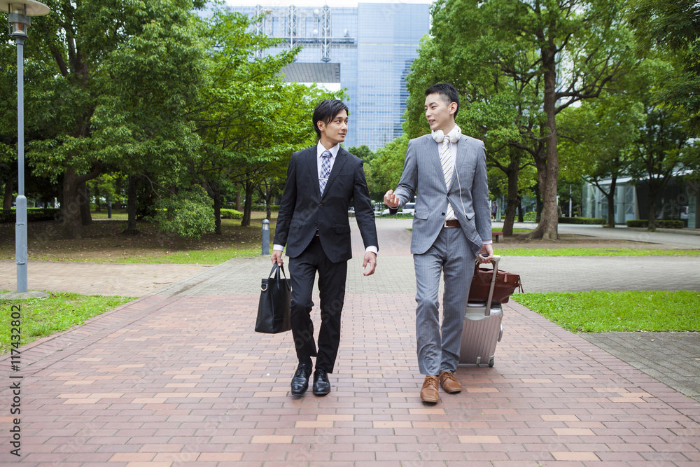 Two young business man is walking in the park while talking