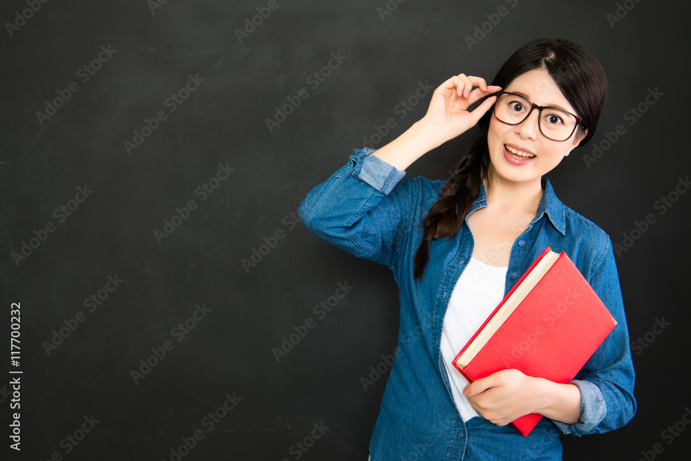 student with glasses and textbook standing in front of blackboar