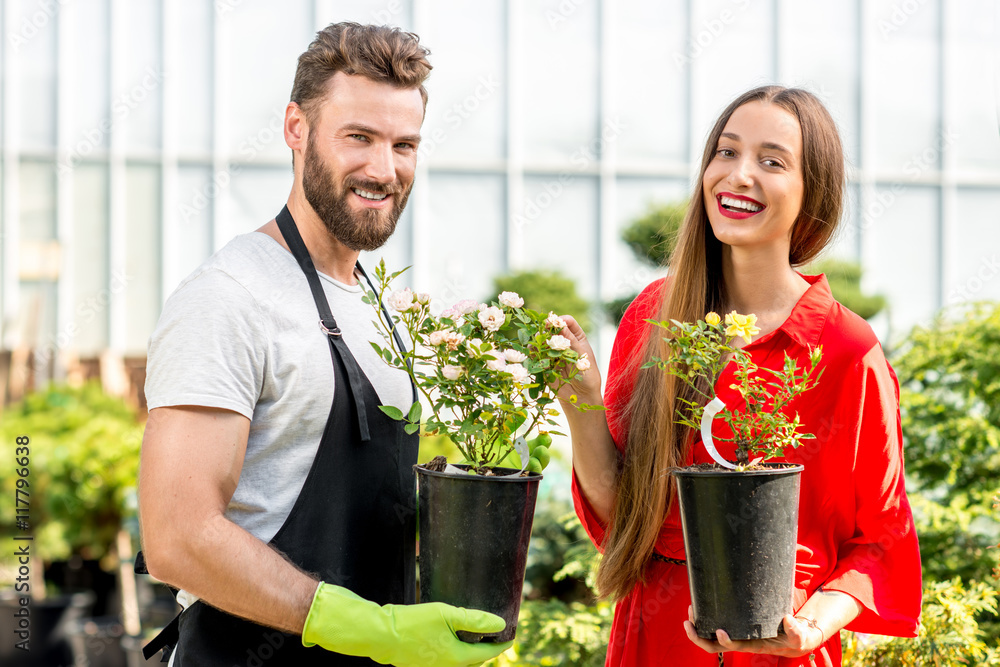 英俊的卖花人站在植物店里帮助女买家选花。顾客