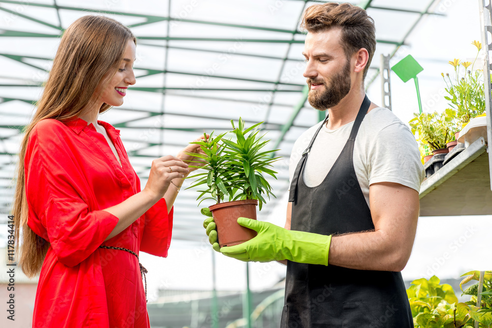 英俊的卖花人站在植物店里帮助女买家选花。顾客