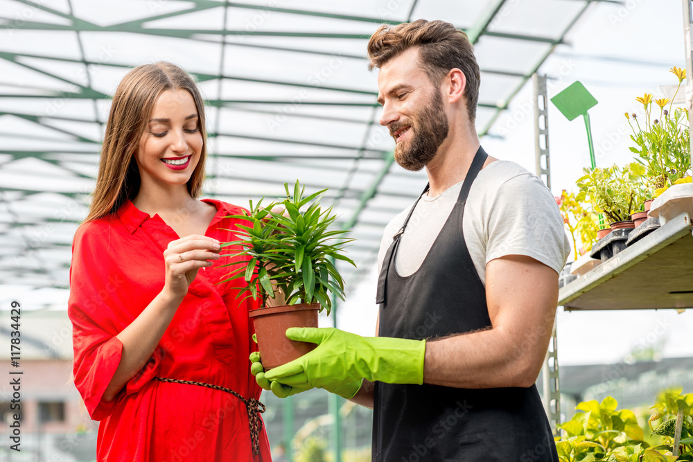 英俊的卖花人站在植物店里帮助女买家选花。顾客