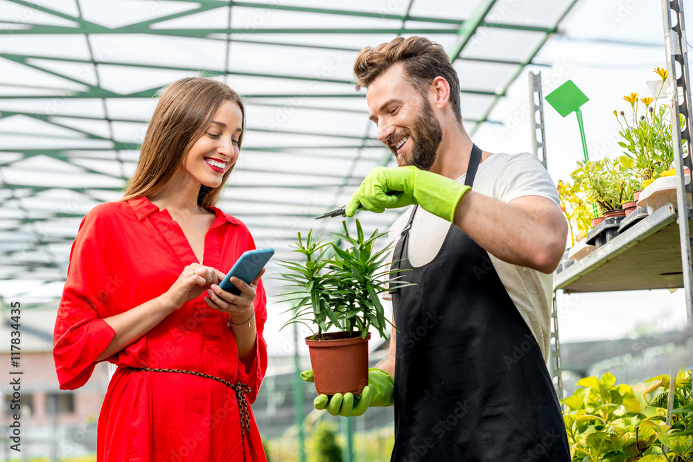 英俊的卖花人站在植物店里帮助女买家选花。女人是我们