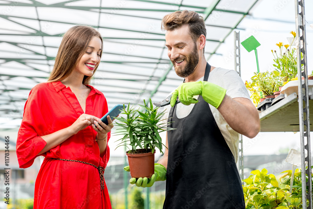 英俊的卖花人站在植物店里帮助女买家选花。女人是我们